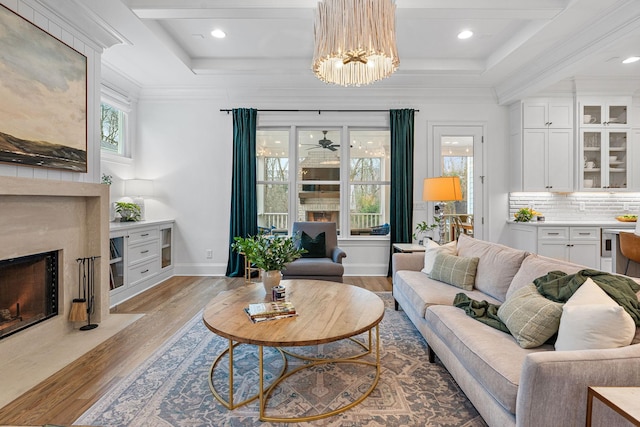 living room featuring a fireplace, ornamental molding, a raised ceiling, and light wood-type flooring