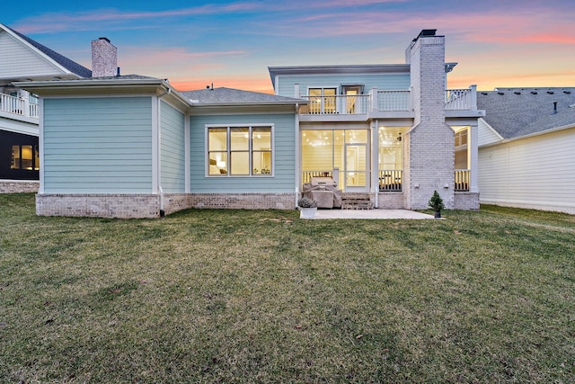 back house at dusk featuring a patio and a lawn