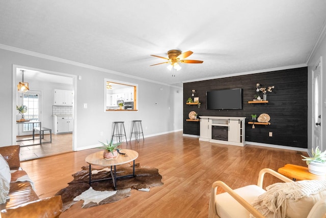 living room featuring crown molding, wood walls, ceiling fan, and light wood-type flooring