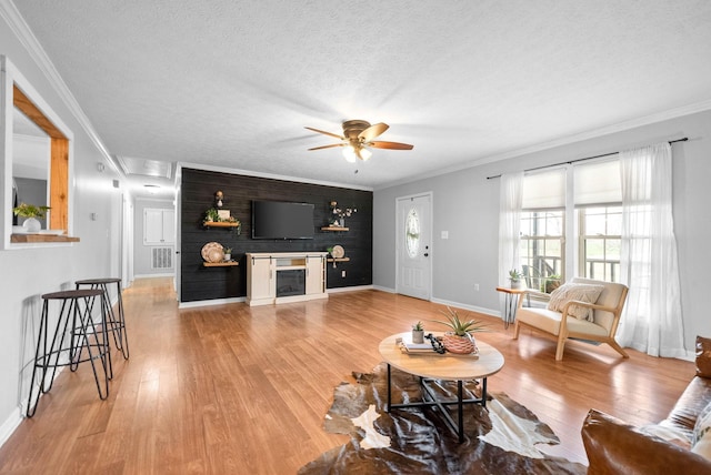 living room with ornamental molding, ceiling fan, a textured ceiling, and light wood-type flooring