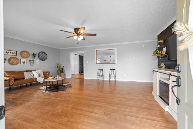 living room featuring ceiling fan, ornamental molding, a textured ceiling, and light wood-type flooring