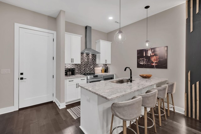 kitchen with wall chimney range hood, sink, light stone countertops, white cabinets, and decorative light fixtures