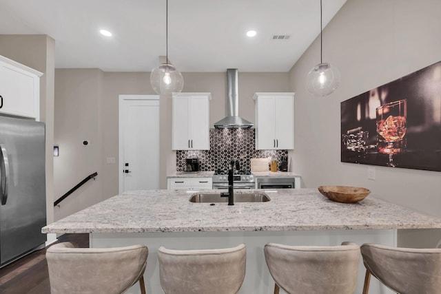 kitchen featuring pendant lighting, wall chimney range hood, light stone counters, and stainless steel fridge