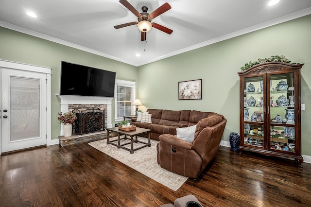 living room with a stone fireplace, ornamental molding, dark hardwood / wood-style floors, and ceiling fan