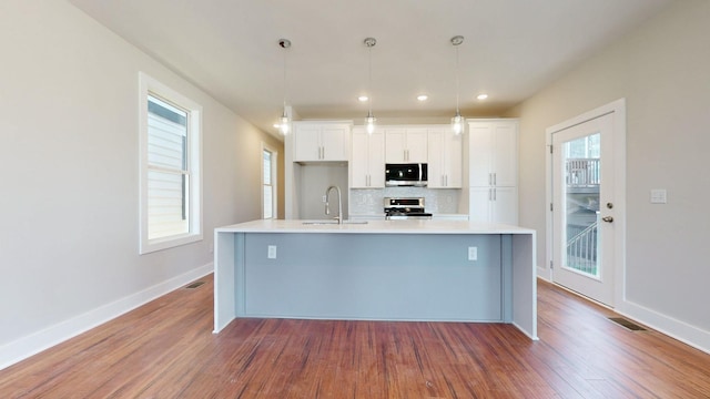 kitchen featuring pendant lighting, sink, stainless steel appliances, white cabinets, and a center island with sink