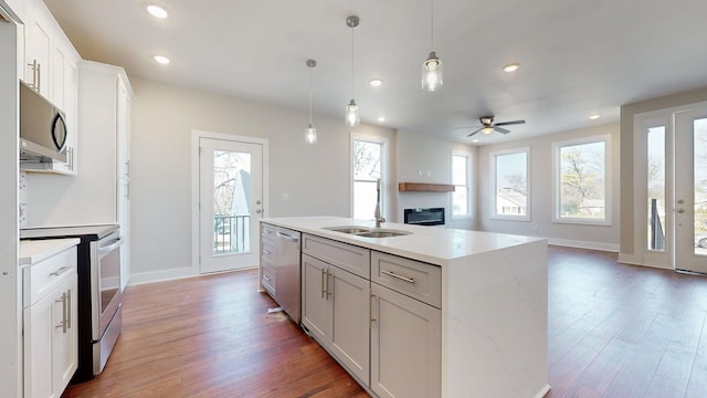 kitchen featuring appliances with stainless steel finishes, sink, white cabinets, hanging light fixtures, and a center island with sink