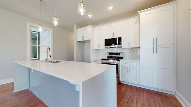 kitchen featuring white cabinetry, sink, hanging light fixtures, stainless steel appliances, and a center island with sink