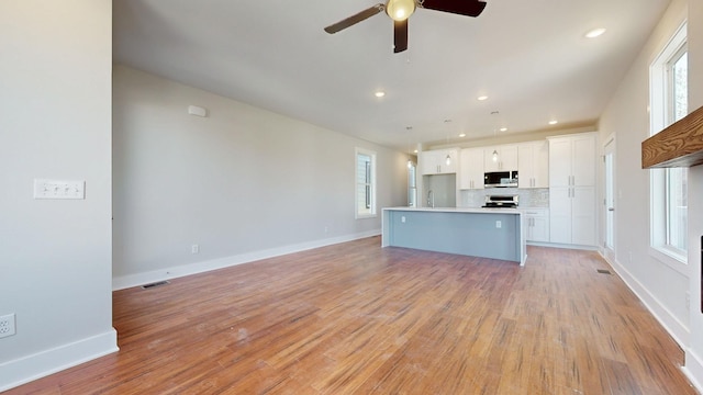 kitchen with pendant lighting, a kitchen island with sink, white cabinets, decorative backsplash, and light wood-type flooring