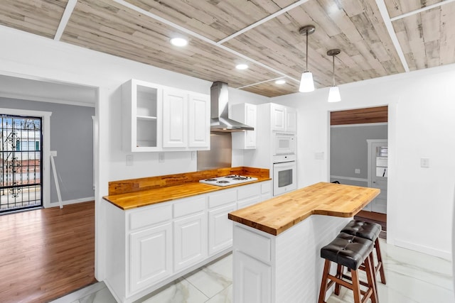 kitchen with butcher block counters, white cabinets, white appliances, and wall chimney exhaust hood