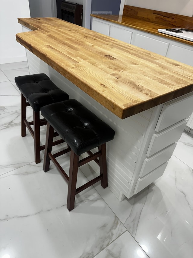 room details with butcher block counters, white cooktop, a center island, white cabinets, and a kitchen bar