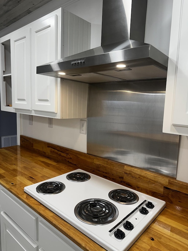 kitchen featuring white cabinetry, wall chimney range hood, white electric cooktop, and wooden counters