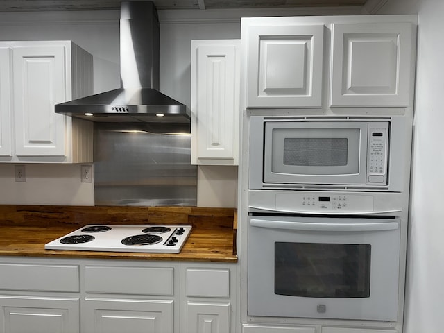 kitchen featuring butcher block counters, white cabinets, white appliances, and wall chimney exhaust hood