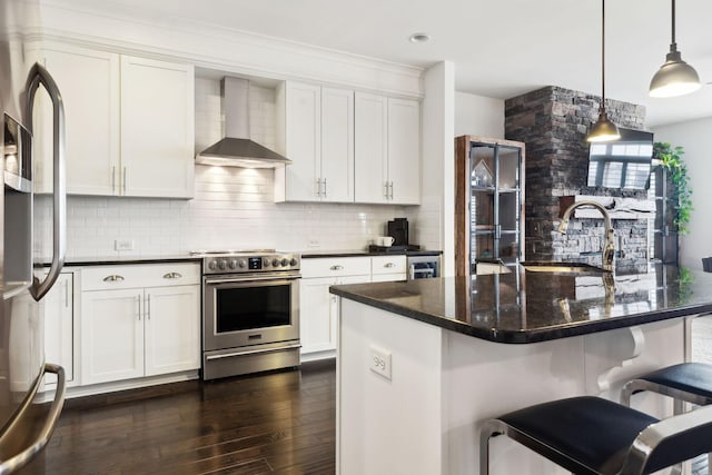 kitchen featuring hanging light fixtures, white cabinetry, appliances with stainless steel finishes, and wall chimney range hood