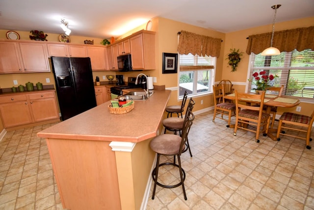 kitchen featuring sink, a breakfast bar, black appliances, decorative light fixtures, and light brown cabinets