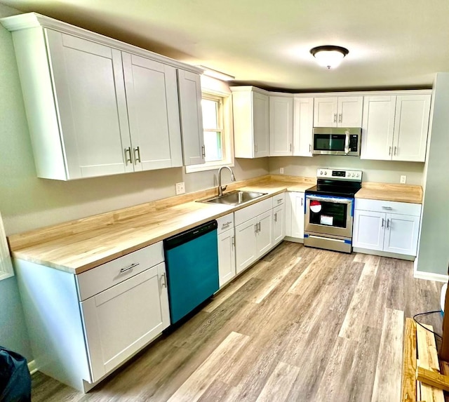 kitchen with sink, butcher block countertops, light hardwood / wood-style flooring, appliances with stainless steel finishes, and white cabinets