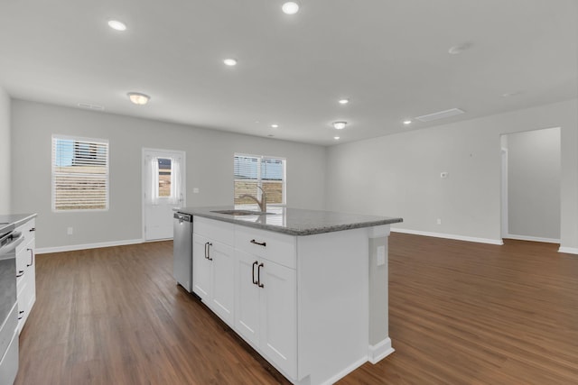 kitchen featuring dark wood-type flooring, dark stone countertops, dishwasher, an island with sink, and white cabinets