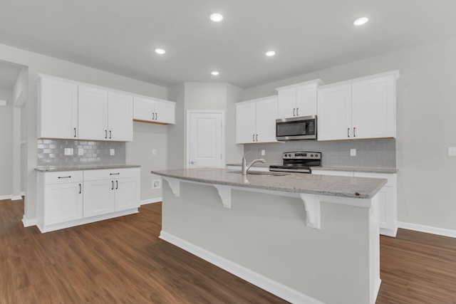 kitchen featuring dark wood-type flooring, sink, white cabinetry, appliances with stainless steel finishes, and an island with sink