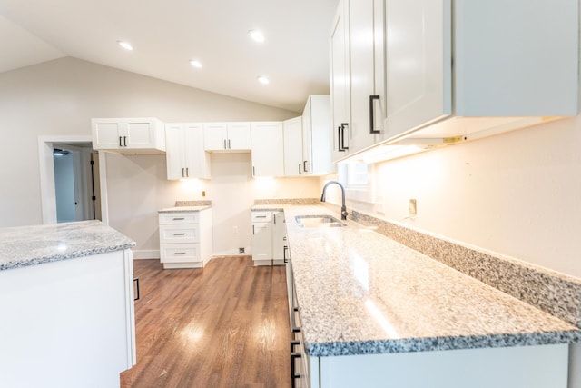 kitchen featuring lofted ceiling, sink, white cabinetry, hardwood / wood-style floors, and light stone countertops