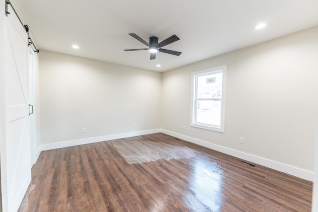 spare room with dark hardwood / wood-style floors, ceiling fan, and a barn door