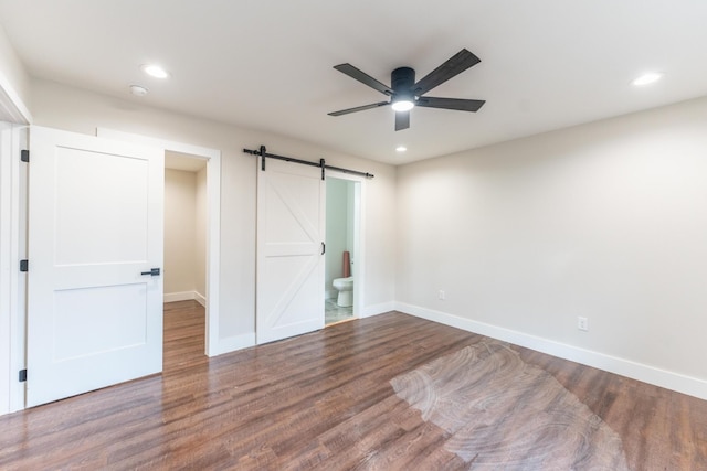 unfurnished bedroom with hardwood / wood-style flooring, ensuite bathroom, a barn door, and ceiling fan