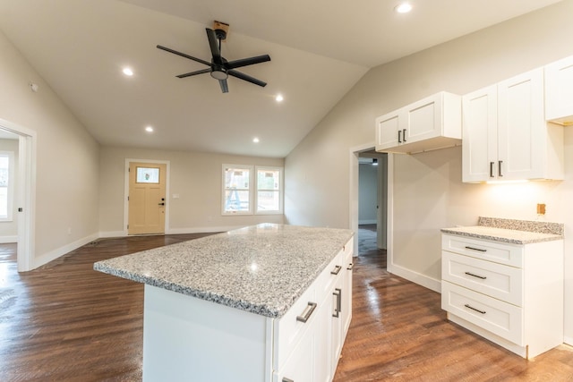 kitchen with lofted ceiling, dark hardwood / wood-style floors, a center island, light stone countertops, and white cabinets