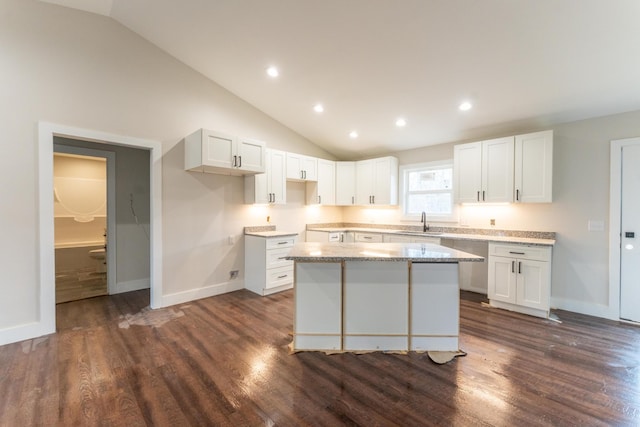 kitchen featuring lofted ceiling, sink, white cabinetry, a center island, and light stone countertops