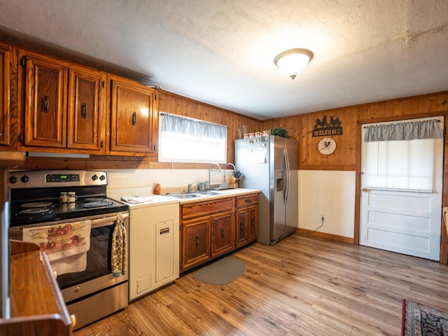 kitchen featuring appliances with stainless steel finishes, wooden walls, sink, and light wood-type flooring