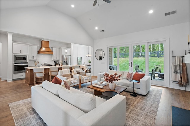 living room with ceiling fan, high vaulted ceiling, and light hardwood / wood-style flooring