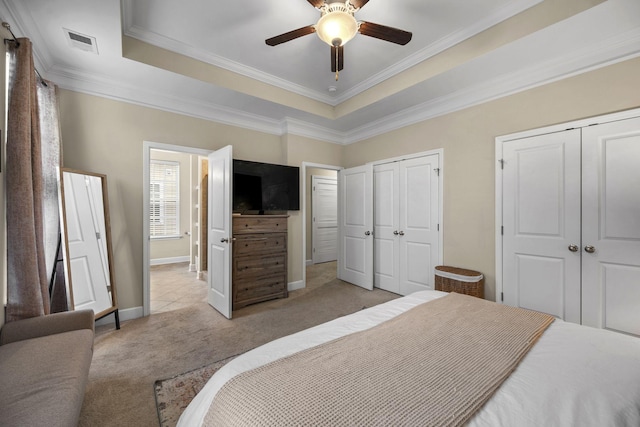 carpeted bedroom featuring ceiling fan, a tray ceiling, ornamental molding, and multiple closets