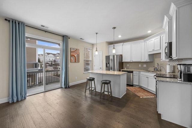 kitchen featuring a kitchen island, a breakfast bar, pendant lighting, white cabinetry, and stainless steel appliances