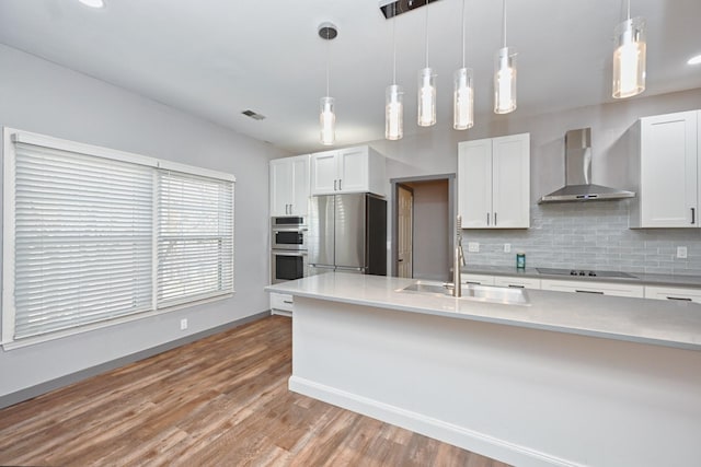 kitchen with wall chimney exhaust hood, sink, white cabinetry, pendant lighting, and stainless steel appliances