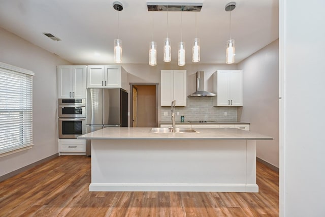 kitchen featuring white cabinetry, sink, an island with sink, and wall chimney exhaust hood