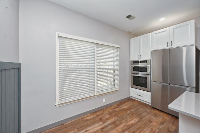 kitchen with stainless steel appliances, white cabinetry, and light hardwood / wood-style flooring