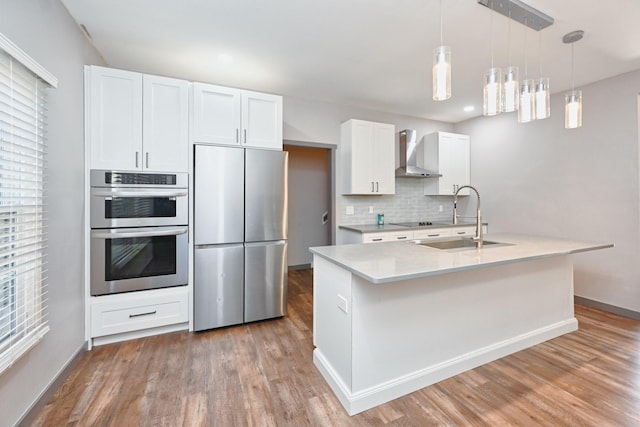 kitchen with appliances with stainless steel finishes, white cabinetry, an island with sink, sink, and wall chimney exhaust hood