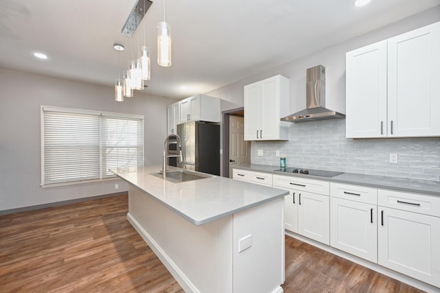 kitchen featuring stainless steel refrigerator, decorative light fixtures, an island with sink, white cabinets, and wall chimney exhaust hood