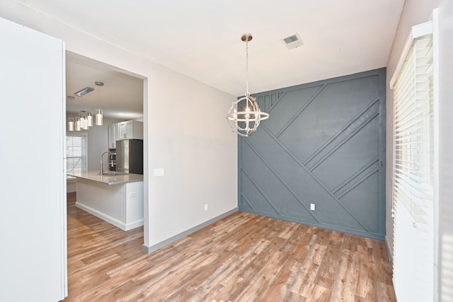 unfurnished dining area featuring sink, a notable chandelier, and light hardwood / wood-style flooring