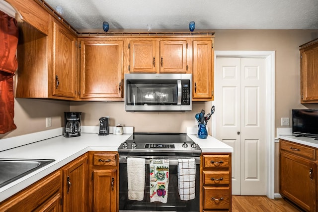 kitchen with stainless steel appliances, sink, a textured ceiling, and light wood-type flooring