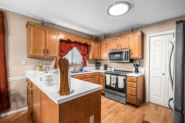 kitchen with sink, stainless steel appliances, light hardwood / wood-style floors, a textured ceiling, and kitchen peninsula