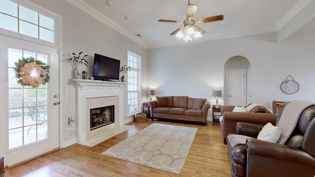 living room with a high end fireplace, light hardwood / wood-style flooring, ornamental molding, and ceiling fan