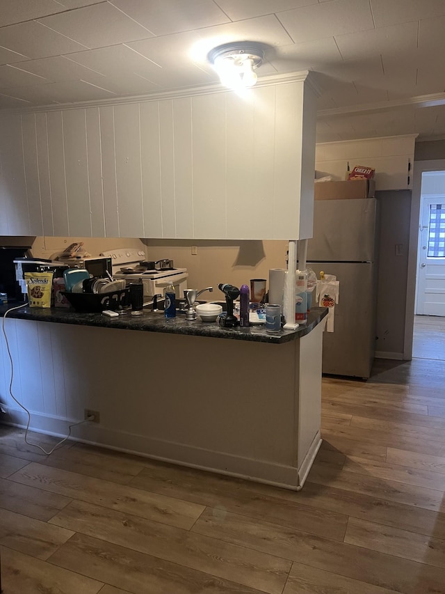 kitchen with white cabinetry, wood-type flooring, stainless steel refrigerator, white electric stove, and kitchen peninsula