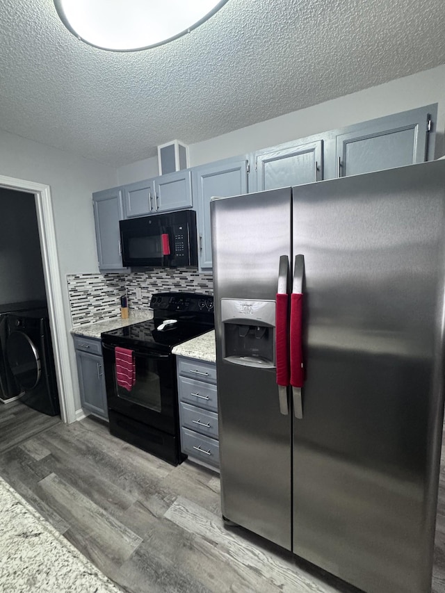 kitchen featuring washer / dryer, black appliances, decorative backsplash, and light wood-type flooring