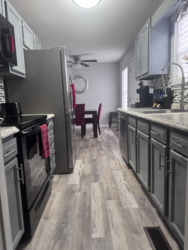 kitchen featuring sink, black electric range oven, stainless steel dishwasher, and gray cabinetry