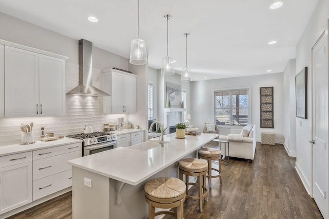 kitchen with sink, a kitchen breakfast bar, wall chimney range hood, a center island with sink, and stainless steel gas range