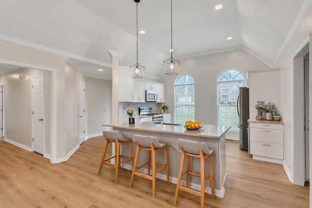 kitchen featuring a breakfast bar, stainless steel appliances, white cabinets, decorative light fixtures, and vaulted ceiling