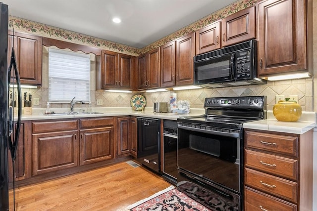 kitchen featuring tasteful backsplash, sink, black appliances, and light wood-type flooring