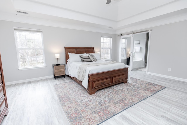 bedroom featuring ensuite bathroom, a barn door, ceiling fan, and light hardwood / wood-style flooring