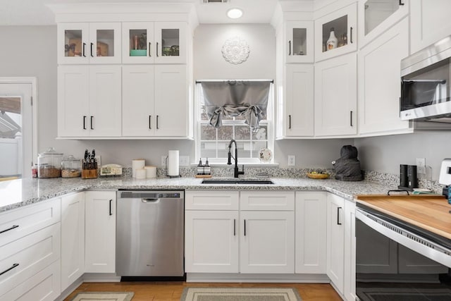 kitchen with light stone countertops, white cabinetry, appliances with stainless steel finishes, and sink