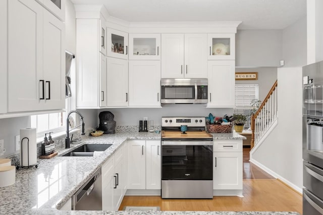 kitchen featuring sink, white cabinetry, light wood-type flooring, appliances with stainless steel finishes, and light stone countertops