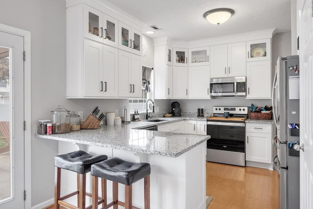 kitchen with sink, white cabinetry, kitchen peninsula, stainless steel appliances, and light stone countertops