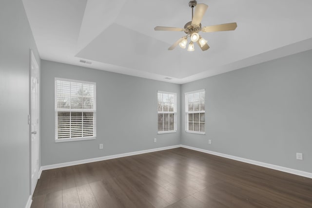 spare room featuring ceiling fan, a tray ceiling, dark wood-type flooring, and a healthy amount of sunlight